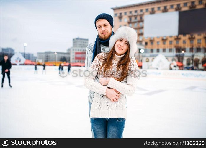 Happy love couple hugs on skating rink. Winter ice-skating on open air, active leisure, man and woman skates together. Happy love couple hugs on skating rink