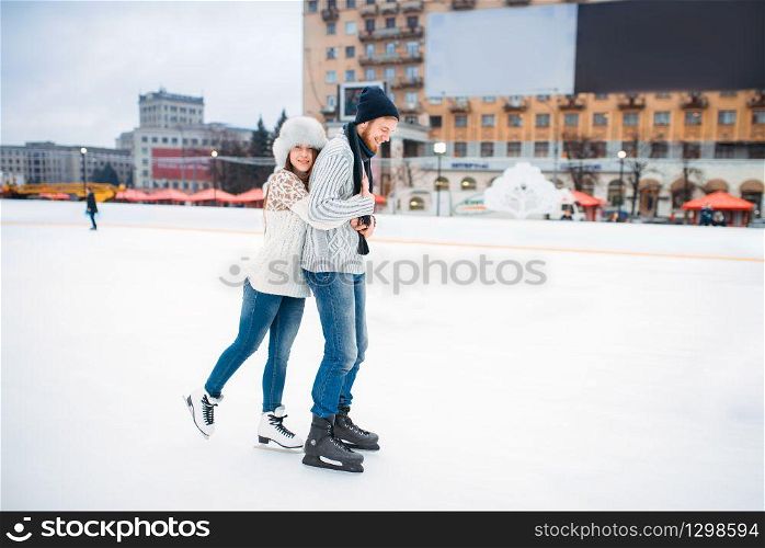 Happy love couple poses on skating rink. Winter ice-skating on open air, active leisure, man and woman skates together