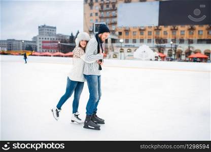 Happy love couple poses on skating rink. Winter ice-skating on open air, active leisure, man and woman skates together