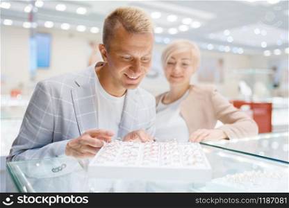 Happy love couple purchase wedding rings in jewelry store. Man and woman choosing gold decoration. Future bride and groom in jewellery shop