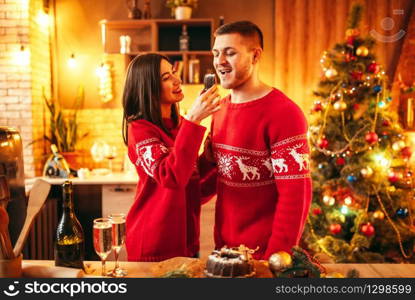 Happy love couple, wife is feeding her husband a christmas cake, festive food. Xmas celebration together, young family happiness. Wife is feeding her husband a christmas cake