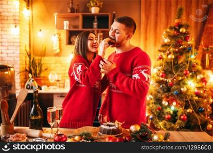 Happy love couple, wife is feeding her husband a christmas cake, festive food. Xmas celebration together, young family happiness