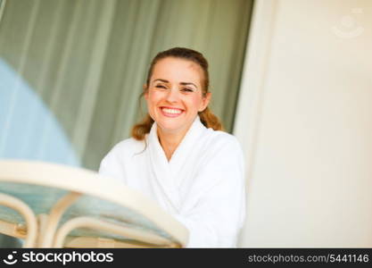 Happy lovely woman in bathrobe sitting at table on terrace &#xA;