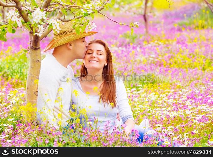 Happy lovers kissing outdoors, romantic date in blooming garden, beautiful young family, affection and love concept