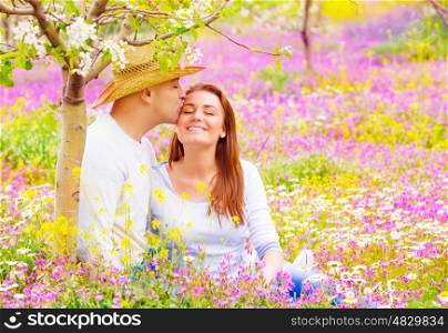 Happy lovers kissing outdoors, romantic date in blooming garden, beautiful young family, affection and love concept