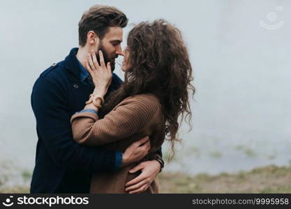 Happy lovers near the lake. Young couple is hugging on autumn day outdoors. A bearded man and curly woman in love. Valentine’s Day. Concept of love and family. Happy lovers near the lake. Young couple is hugging on autumn day outdoors. A bearded man and curly woman in love. Valentine’s Day. Concept of love and family.
