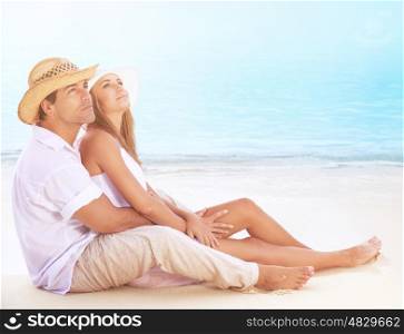 Happy lovers on the beach, beautiful young couple sitting on sandy coast and hugging, dreamy looking up in the sky and enjoying romantic honeymoon