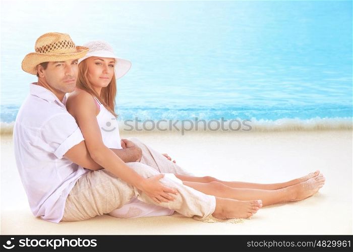 Happy lovers on the beach, beautiful young couple sitting on sandy coast and hugging, enjoying each other and romantic honeymoon vacation