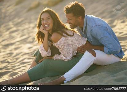 Happy loving couple laughing together sitting on the sand of the beach. Young couple laughing together sitting on the sand of the beach