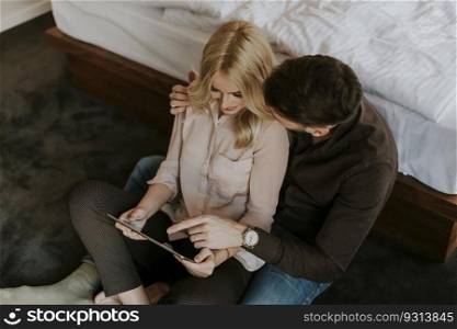 Happy loving couple sitting on the floor with digital tablet
