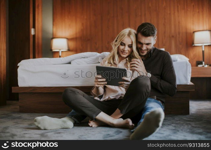 Happy loving couple sitting on the floor with digital tablet