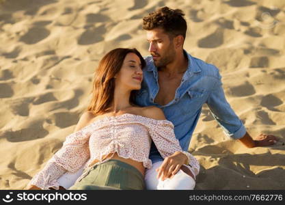 Happy loving couple sitting on the sand of the beach enjoying each other. Attractive couple sitting on the sand of the beach enjoying each other