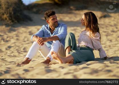 Happy loving couple sitting on the sand of the beach looking at the horizon.. Attractive couple sitting on the sand of the beach