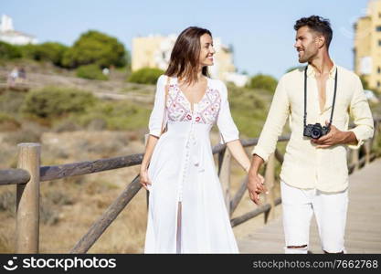 Happy loving couple walking along a wooden path towards the beach in a coastal area.. Loving couple walking along a wooden path towards the beach in a coastal area.