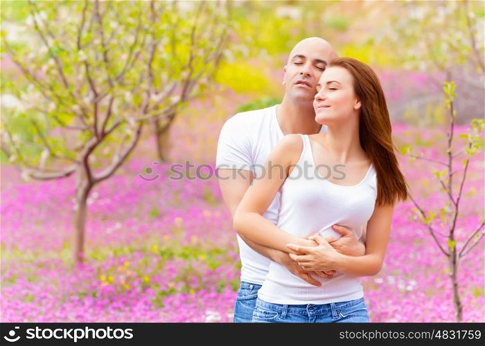 Happy loving family hugging in spring park on beautiful pink floral meadow, enjoying each other with closed eyes, springtime weekend, love concept&#xA;