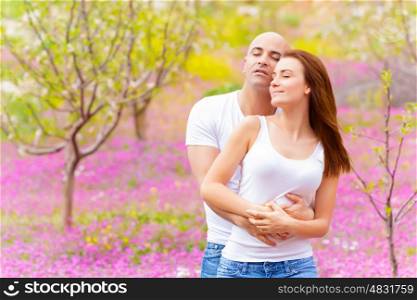 Happy loving family hugging in spring park on beautiful pink floral meadow, enjoying each other with closed eyes, springtime weekend, love concept&#xA;