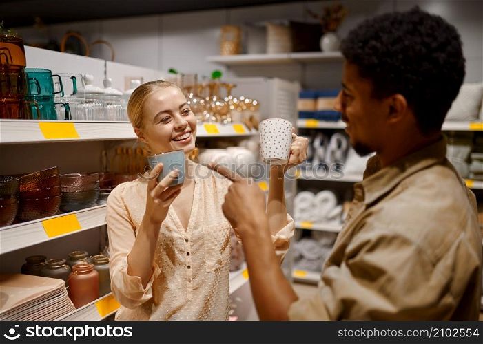 Happy loving just married couple choosing ceramic cups at household goods supermarket department. Loving couple choosing ceramic cups at shop