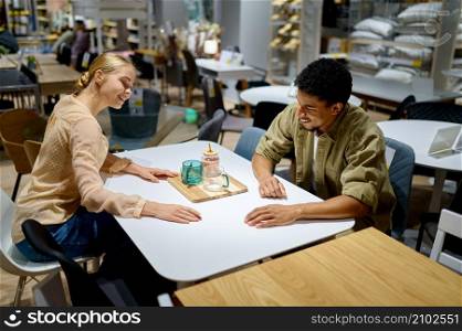 Happy loving multiracial couple looking for kitchen table in shop. Furniture store interior. Multiracial couple looking for table in shop