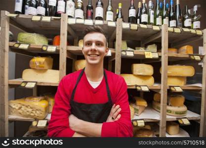 Happy male clerk standing against shelves in cheese shore