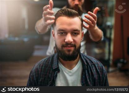 Happy male client after making hairstyle at the barbershop, coiffeur on background