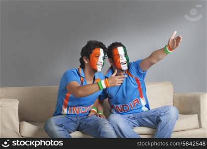 Happy male friends with face painted in Indian tricolor looking away while sitting on sofa