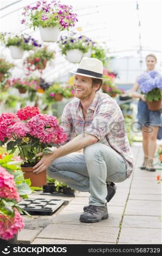 Happy male gardener holding flower pot with colleague standing in background at greenhouse