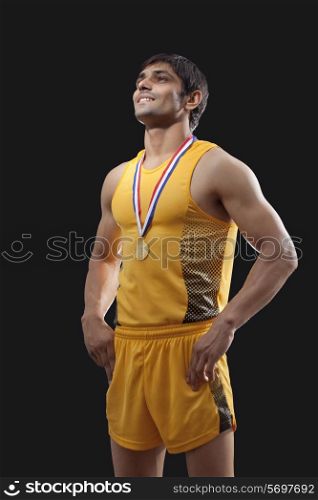 Happy male gold medalist standing with hands on waist over black background