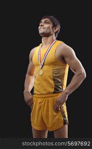 Happy male gold medalist standing with hands on waist over black background
