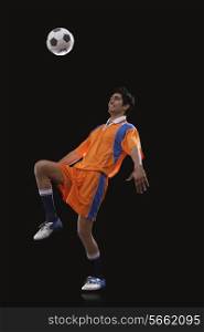 Happy male Indian soccer player doing kick ups isolated over black background