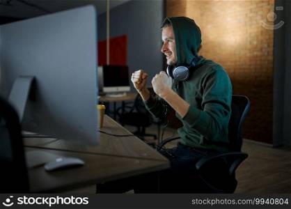Happy male internet hacker in hood and headphones. Illegal web programmer at workplace, criminal occupation. Data hacking, cyber security. Happy male internet hacker in hood and headphones