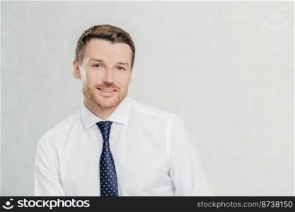 Happy male office worker with friendly smile, dressed elegantly, thinks about future plans, involved in business, prepares for meeting, poses alone against white background. Professional man leader