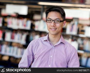 Happy male student at the library. Happy male asian student wearing glasses standing at the library