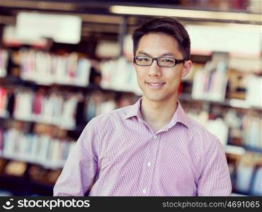 Happy male student at the library. Happy male asian student wearing glasses standing at the library