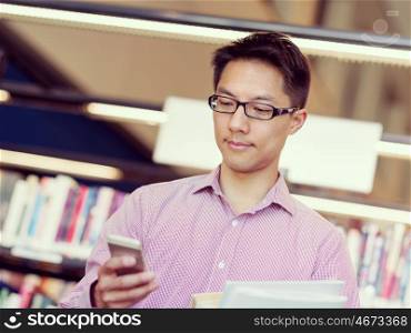 Happy male student holding books at the library. Happy male asian student holding books and his mobile at the library