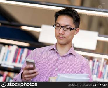 Happy male student holding books at the library. Happy male asian student holding books and his mobile at the library