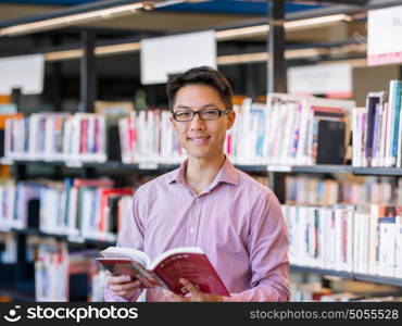 Happy male student holding books at the library. Happy male asian student holding books at the library