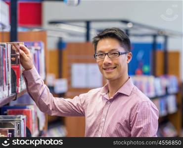 Happy male student picking up books at the library. Happy male asian student holding books at the library