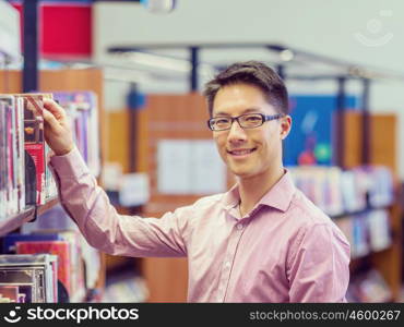 Happy male student picking up books at the library. Happy male asian student holding books at the library