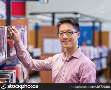 Happy male student picking up books at the library. Happy male asian student holding books at the library