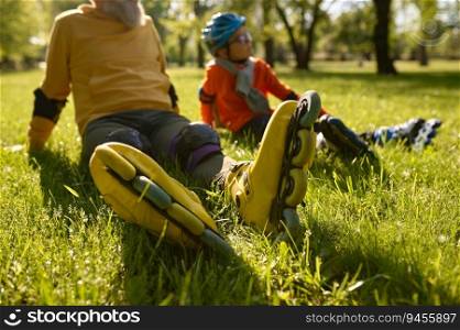 Happy man and boy rollerskaters rest on grass filed in park. Young and adult people having active leisure activity and fun sports time together. Happy man and boy rollerskaters rest on grass filed in park