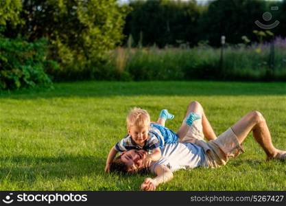 Happy man and child having fun outdoor on meadow. Family lifestyle scene of father and son resting together on green grass in the park.