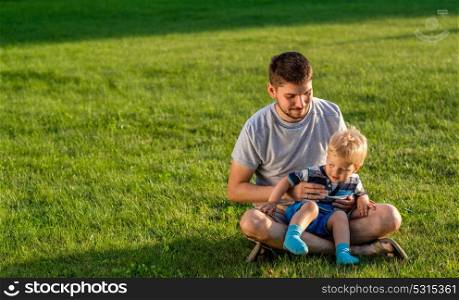 Happy man and child having fun outdoor on meadow. Family lifestyle scene of father and son resting together on green grass in the park.