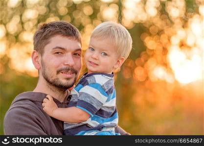 Happy man and his child having fun outdoors. Family lifestyle rural scene of father and son in sunset sunlight. 