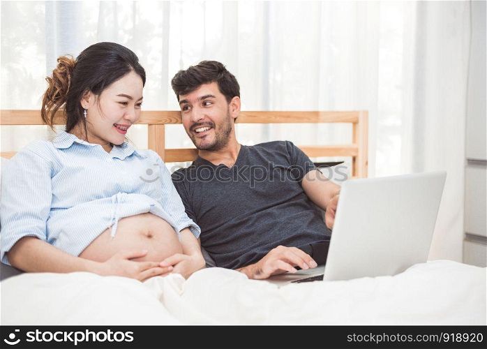 Happy man and his pregnant wife using laptop to searching newborn baby items for preparing parenthood. Couple lifestyle family and technology concept. Women health and medical theme.