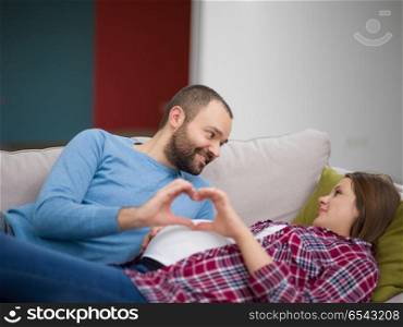 Happy man and pregnant woman showing heart sign with fingers while relaxing on the sofa at home. man and pregnant woman showing heart sign
