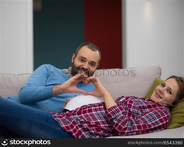 Happy man and pregnant woman showing heart sign with fingers while relaxing on the sofa at home. man and pregnant woman showing heart sign
