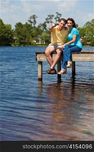Happy Man and Woman Couple Sitting On A Pier By Lake