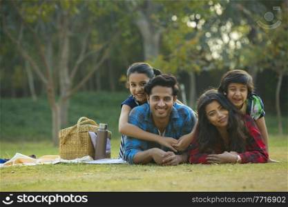Happy man and woman on a picnic lying down in garden beside a picnic basket and their children lying on their backs.