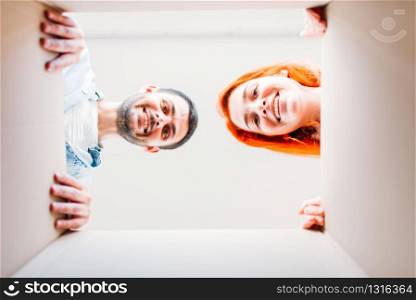 Happy man and woman, view from inside the cardboard box, moving to new house. Young couple, housewarming. Man and woman, view from inside the cardboard box