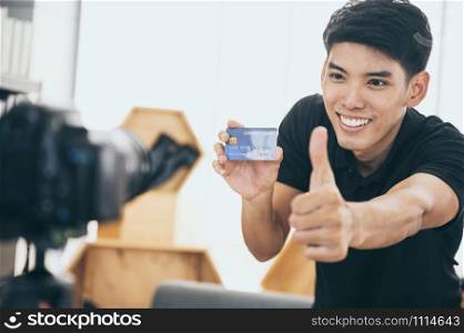 Happy man at home speaking in front of camera for vlog. Young Asian man working as blogger, recording video tutorial for Internet
